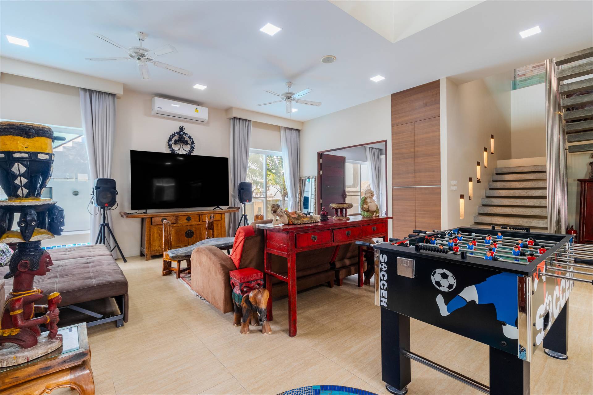 Spacious entertainment lounge with large flat-screen TV, foosball table, and eclectic Thai decor