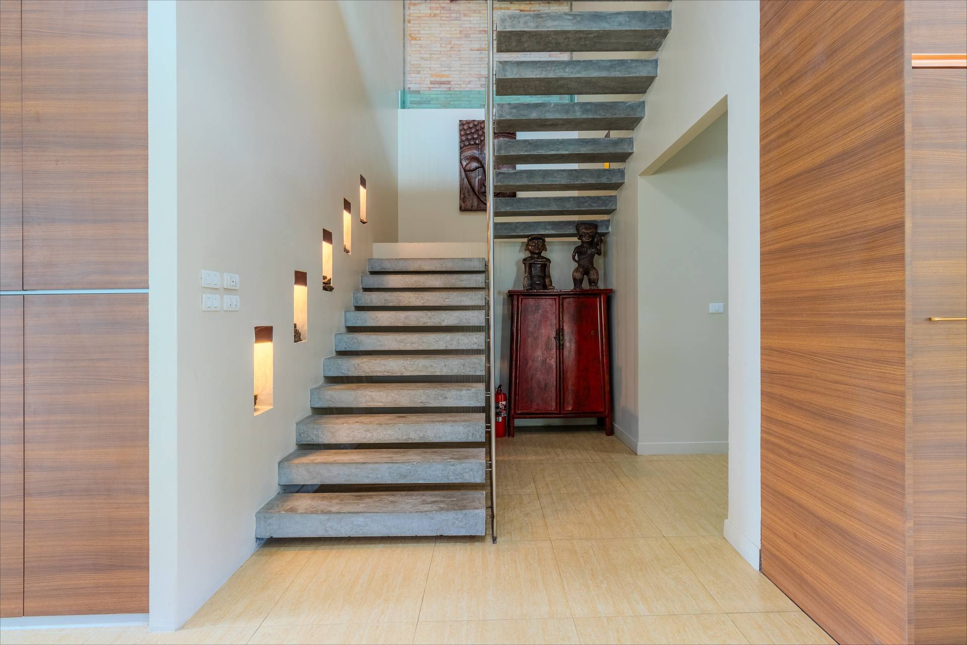 Modern floating concrete staircase with recessed wall lighting and carved wood accents