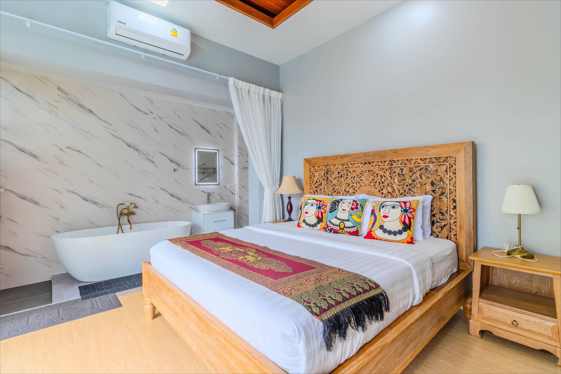 Elegant bedroom with carved teak headboard, freestanding bathtub, and marble-effect wall