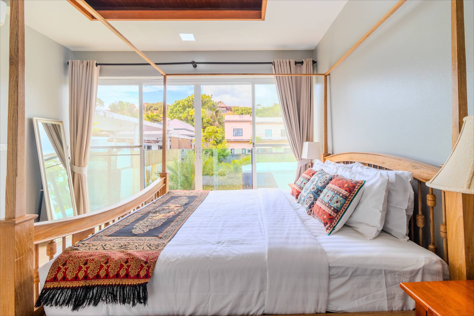 Four-poster teak bed with Thai silk runner and pool-view balcony in Rawai villa bedroom