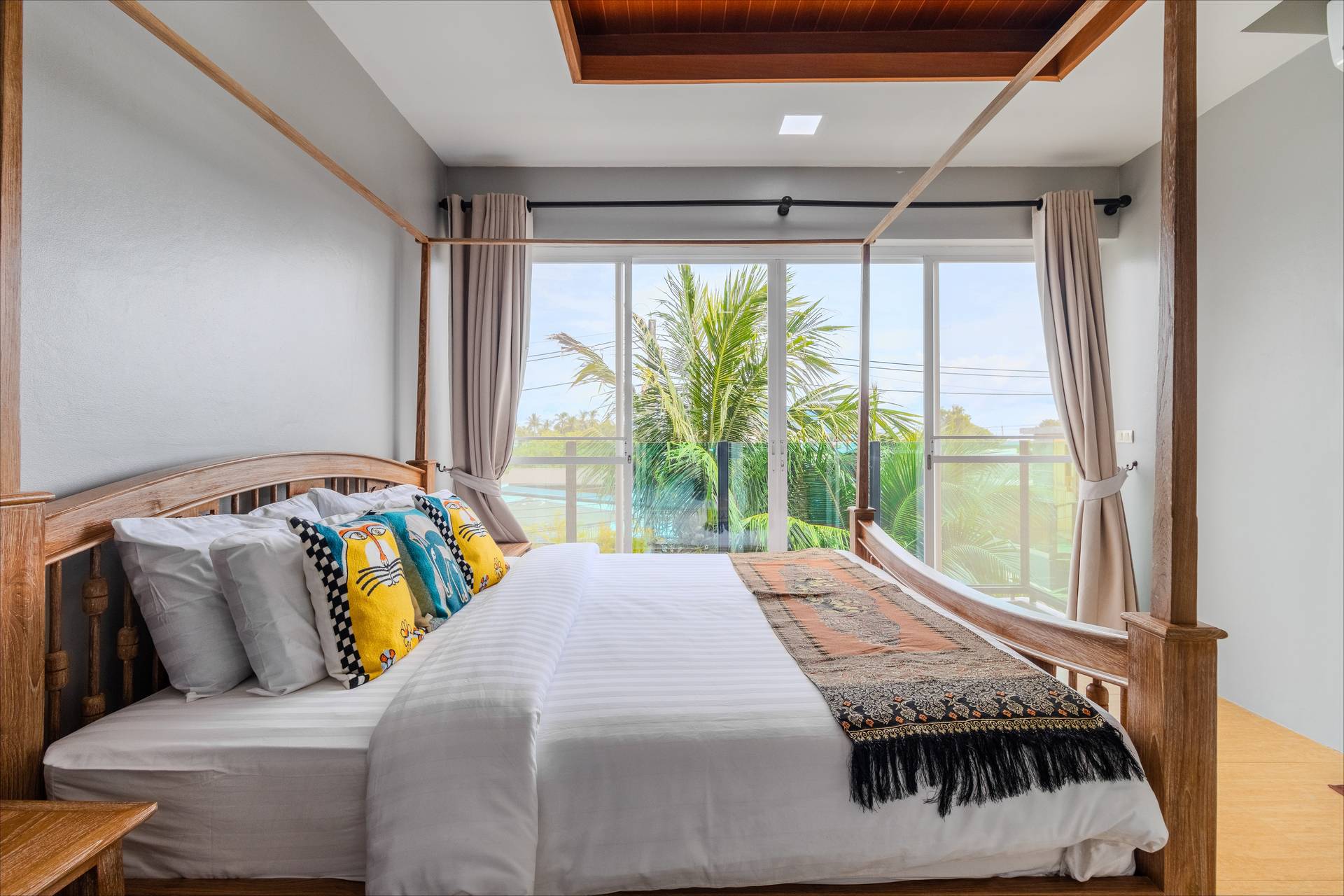 Bright four-poster bedroom with tropical garden views and colorful art cushions