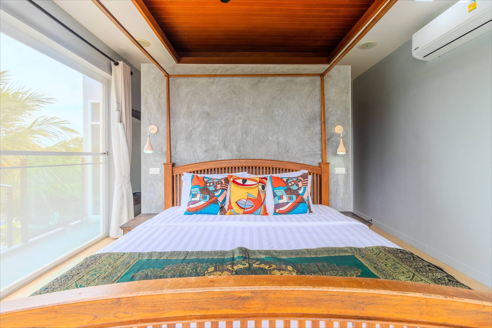 Teak four-poster bed with concrete feature wall, wooden ceiling, and balcony palm tree views
