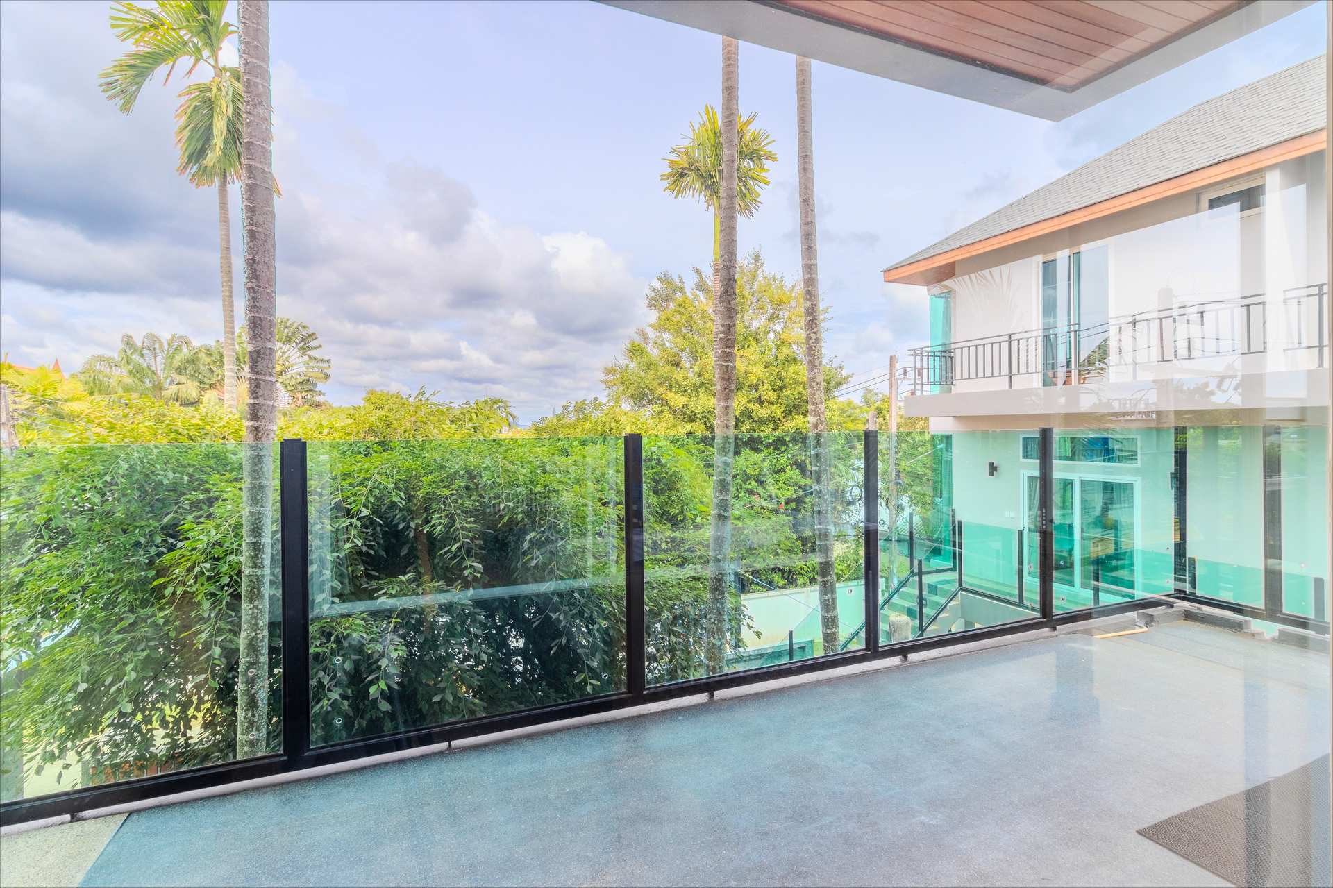 Glass-railed upper terrace overlooking tropical gardens and villa pool area with palm trees