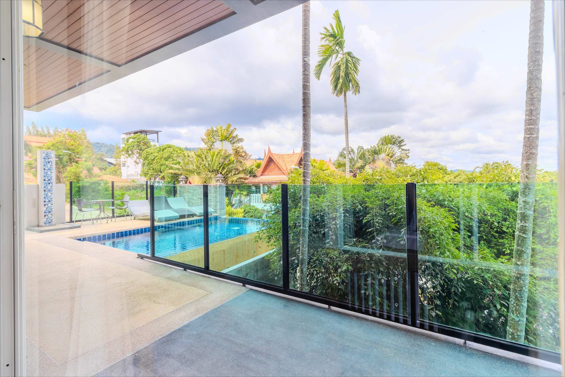 Balcony view of rooftop infinity pool with sun loungers and traditional Thai temple rooftop backdrop