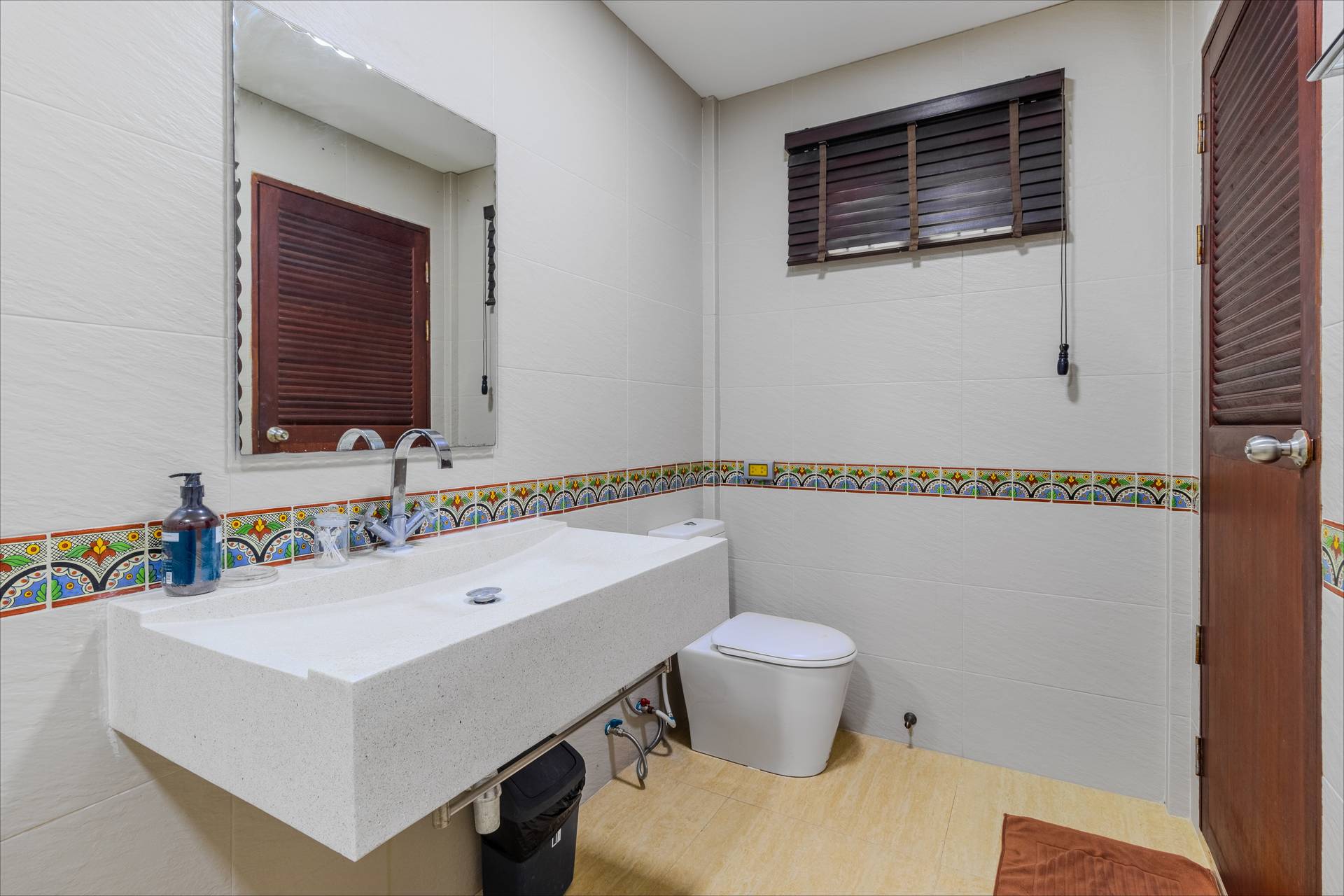 Modern en-suite bathroom with decorative tile border, stone vanity, and wooden shutters