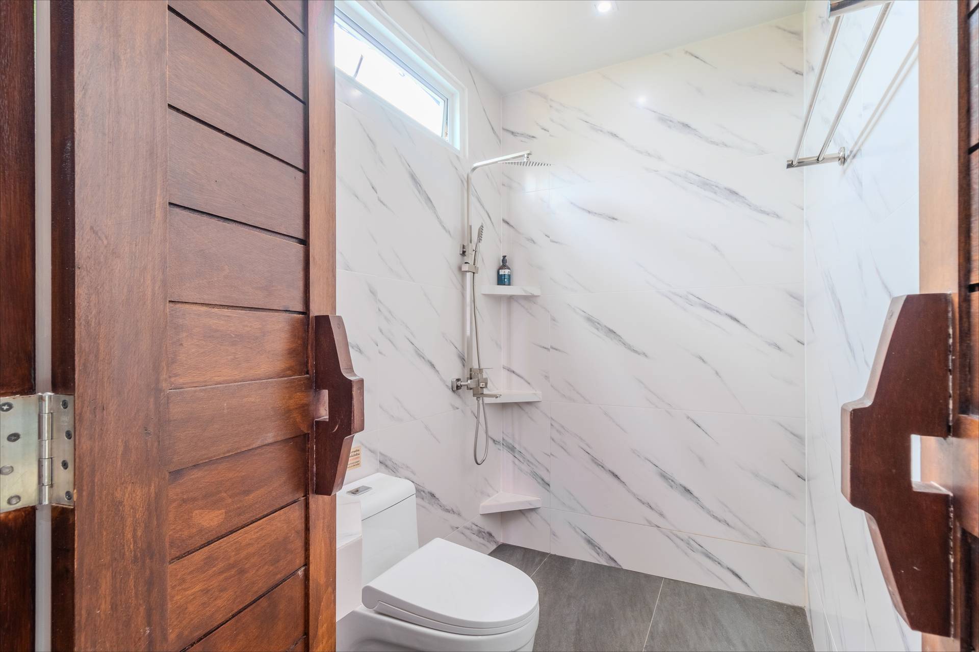 Marble-tiled walk-in shower with rain head and teak wood doors in villa en-suite