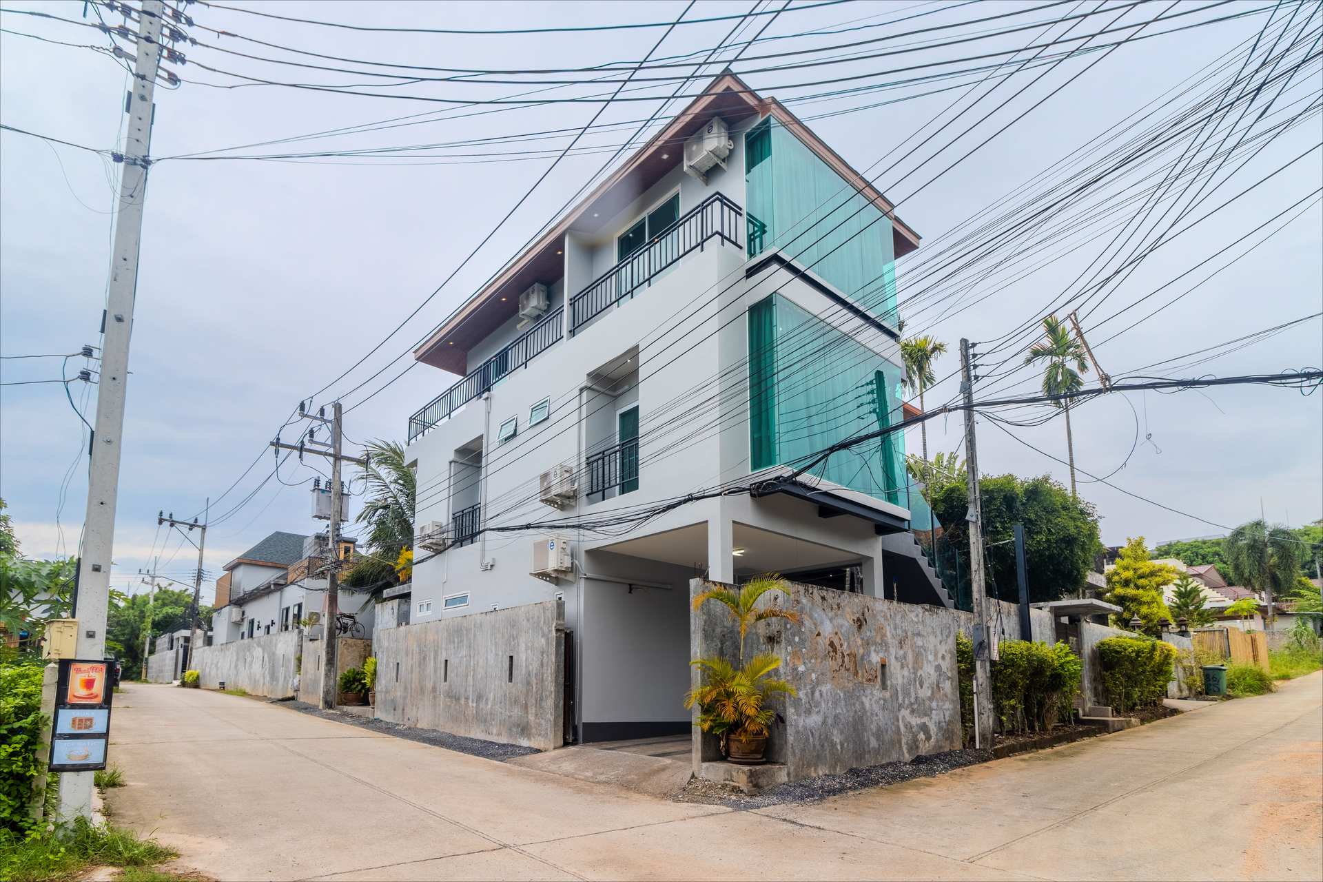 Street view of modern three-storey luxury villa with turquoise glass balconies in Rawai Phuket