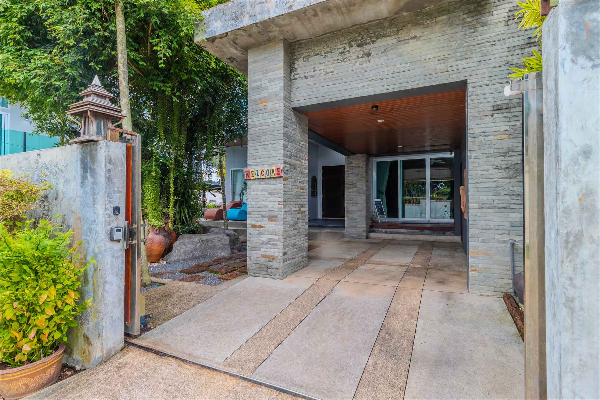 Contemporary stone-clad entrance portico with welcome sign and covered carport at Rawai villa