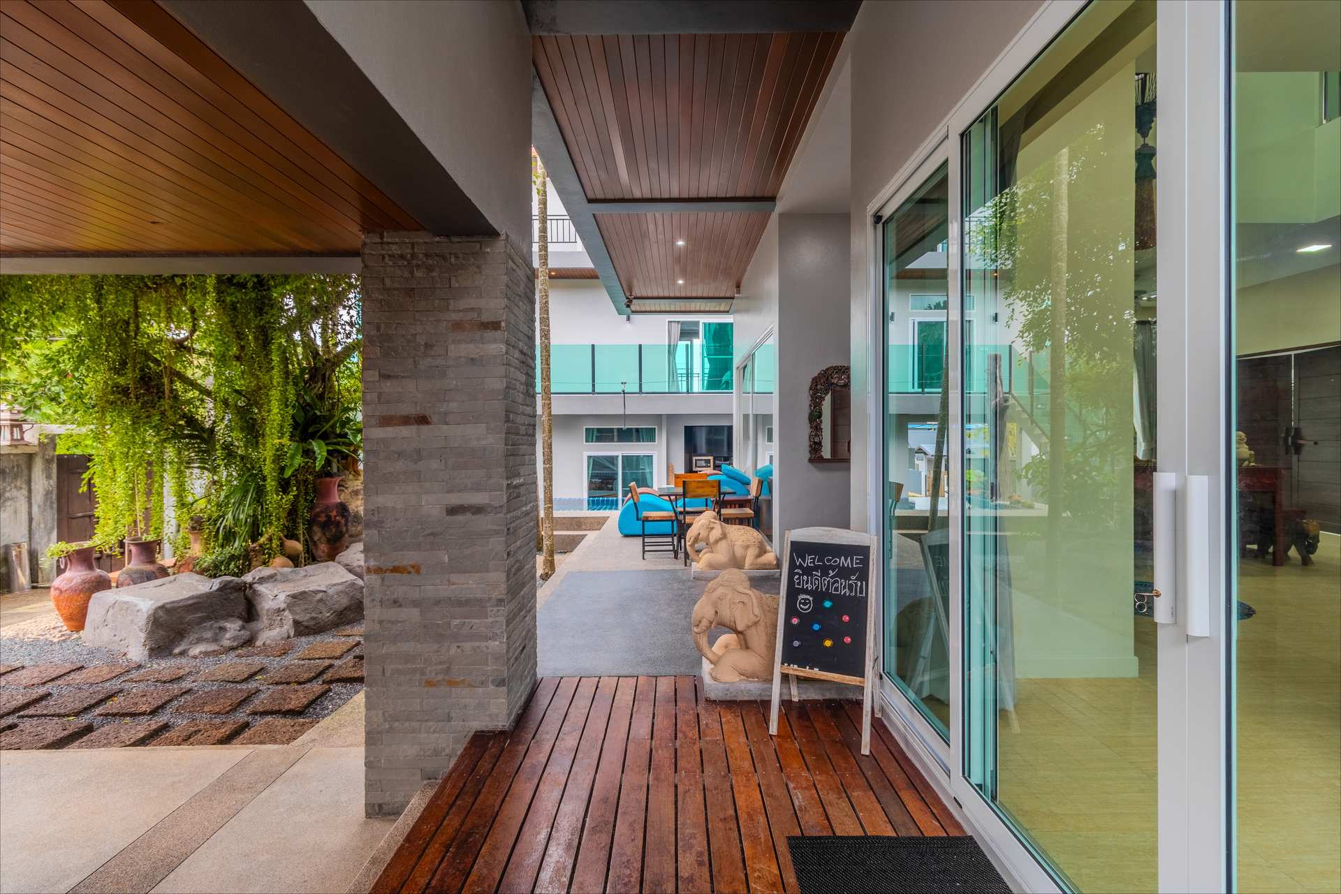 Covered wooden deck walkway with welcome chalkboard, elephant statues, and garden courtyard views