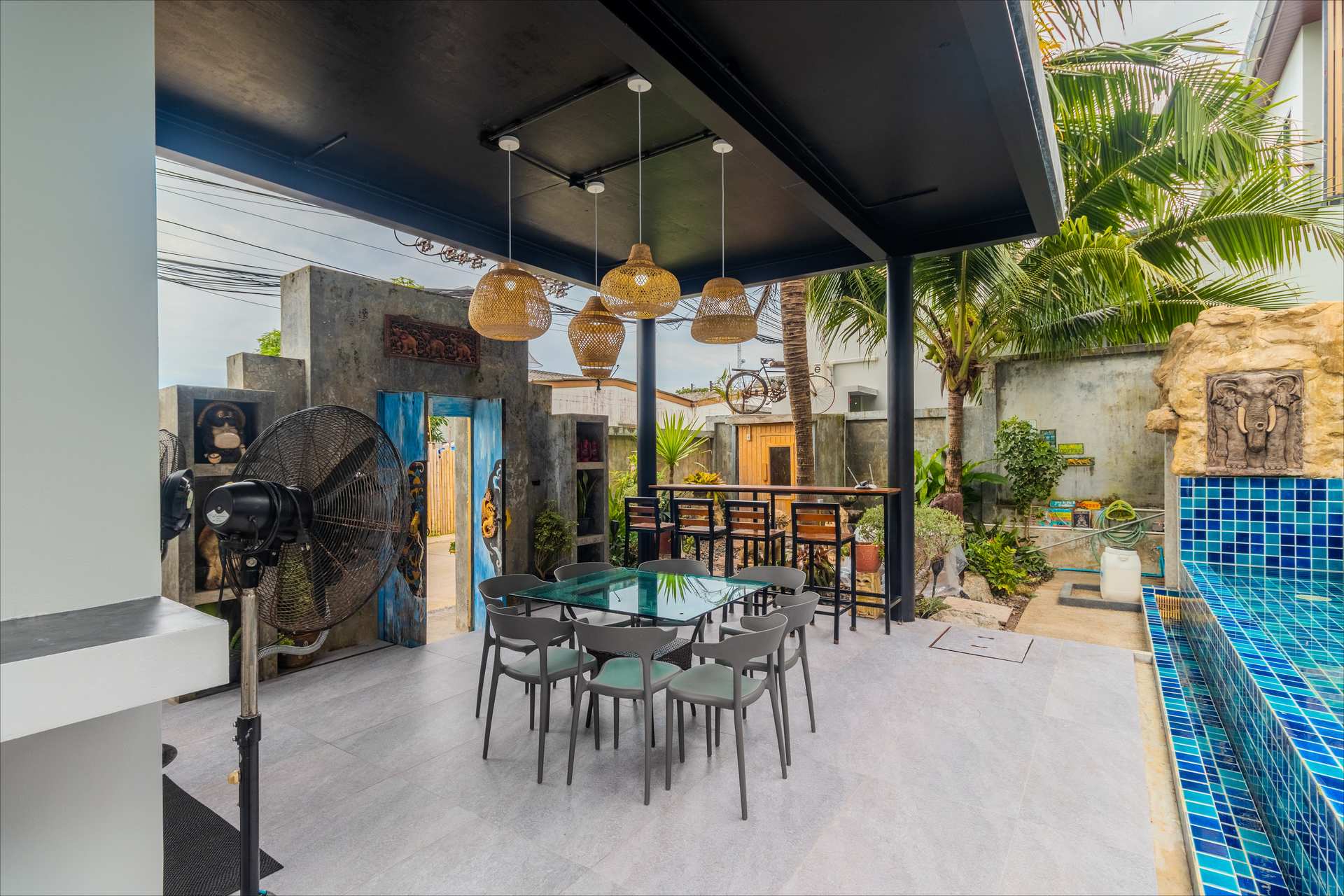Covered outdoor dining area with rattan pendant lights and poolside seating