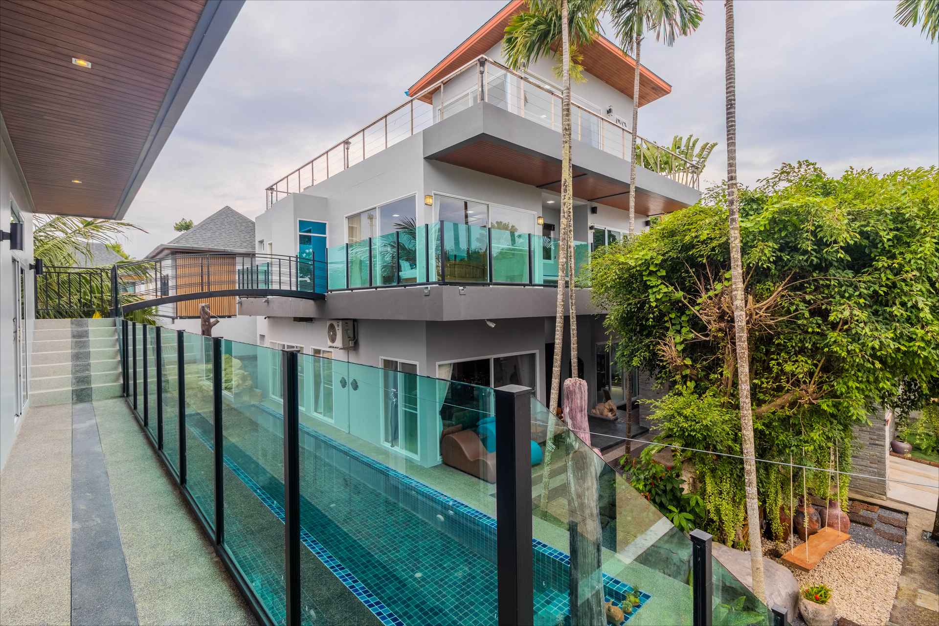 Multi-level villa exterior with turquoise glass-walled pool and lush tropical landscaping