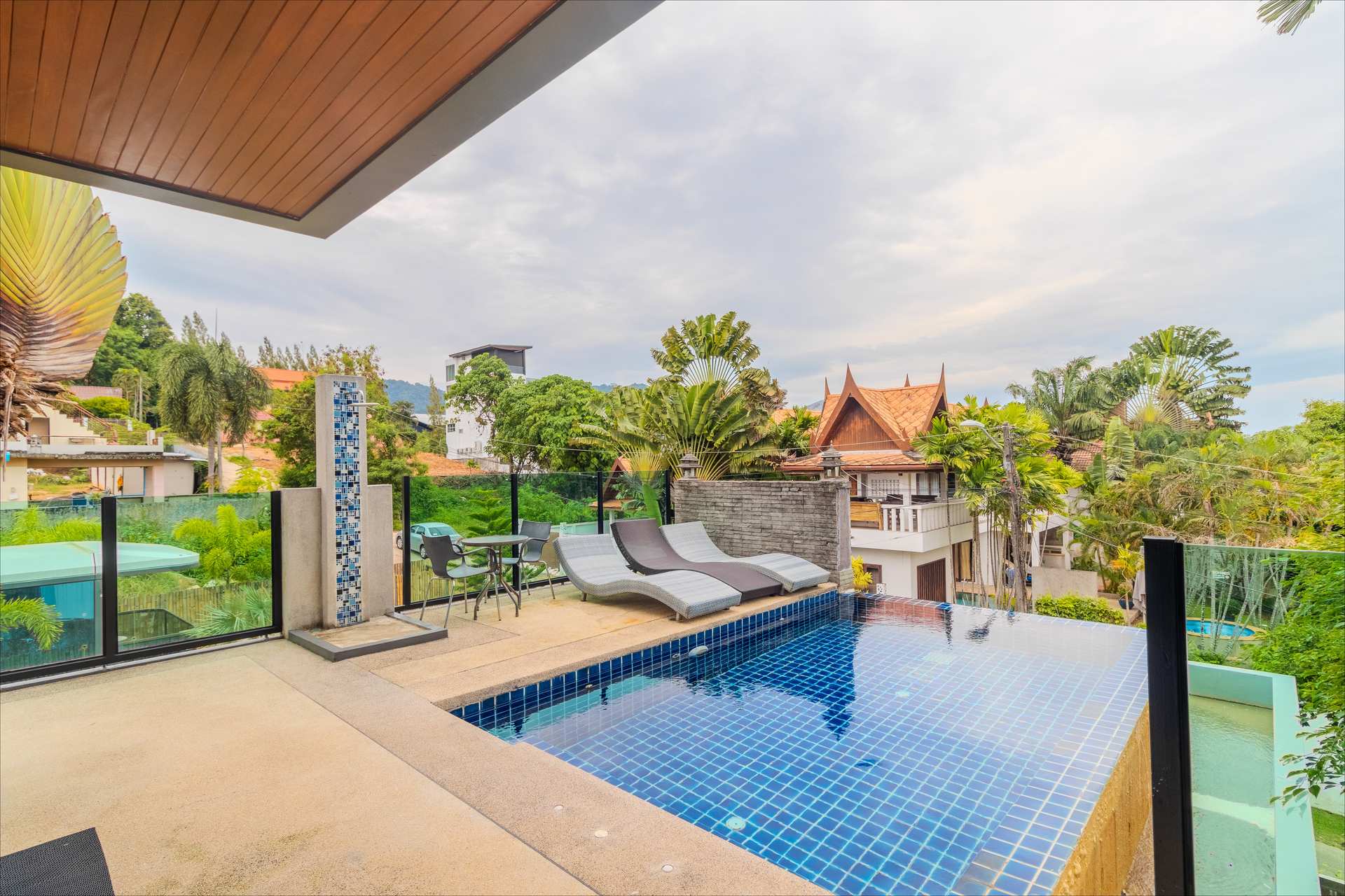 Rooftop infinity pool with sun loungers, outdoor shower, and panoramic Rawai hillside views at dusk