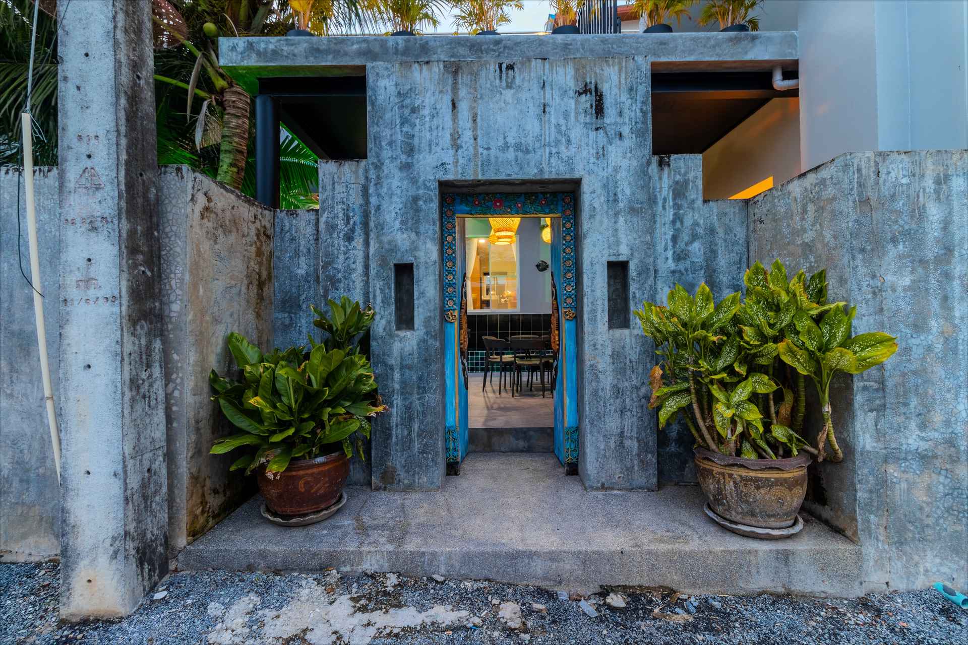 Industrial concrete garden entrance with turquoise door, potted plants, and evening lighting