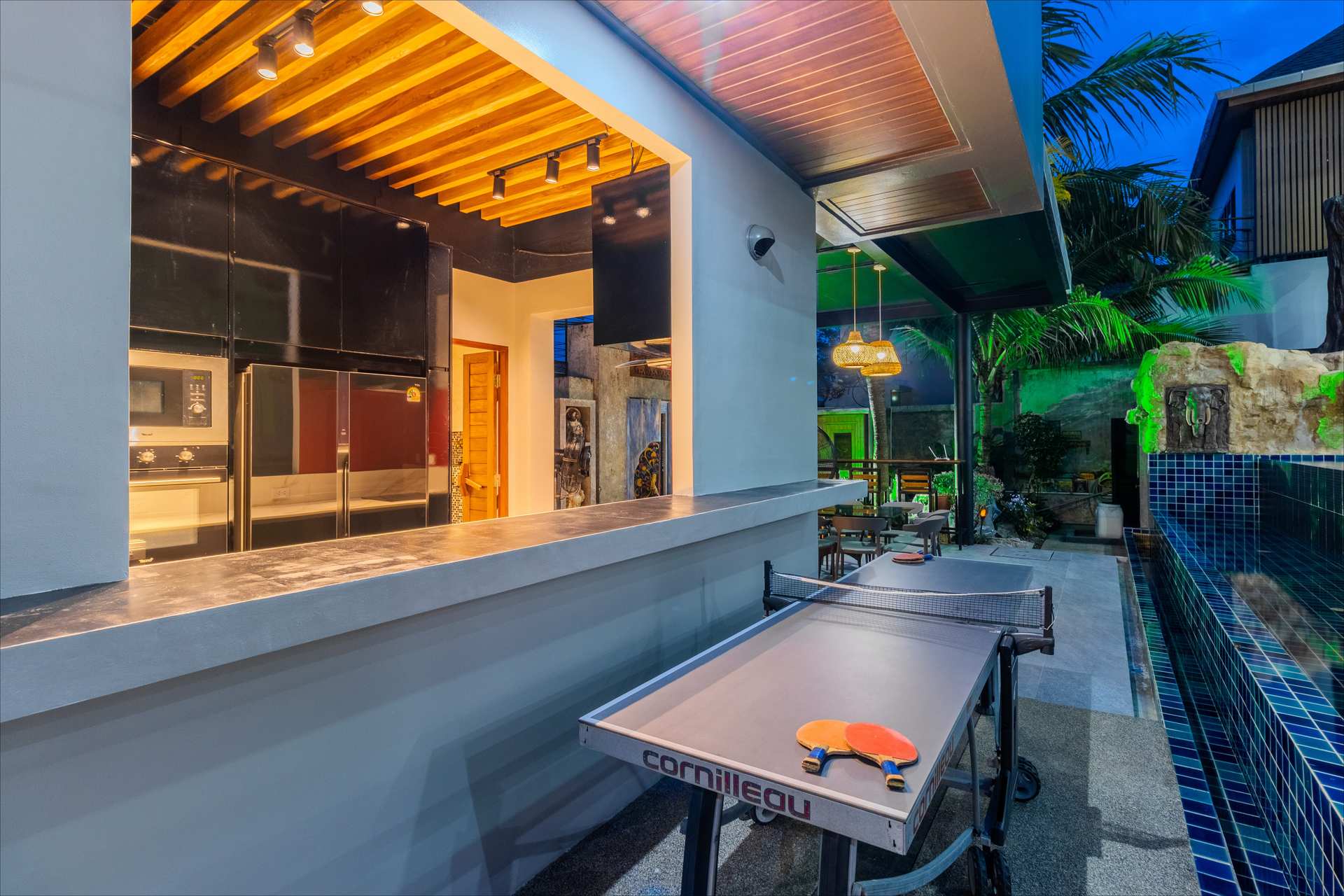 Blue-tiled rooftop pool illuminated at twilight with tropical garden surroundings in Phuket villa
